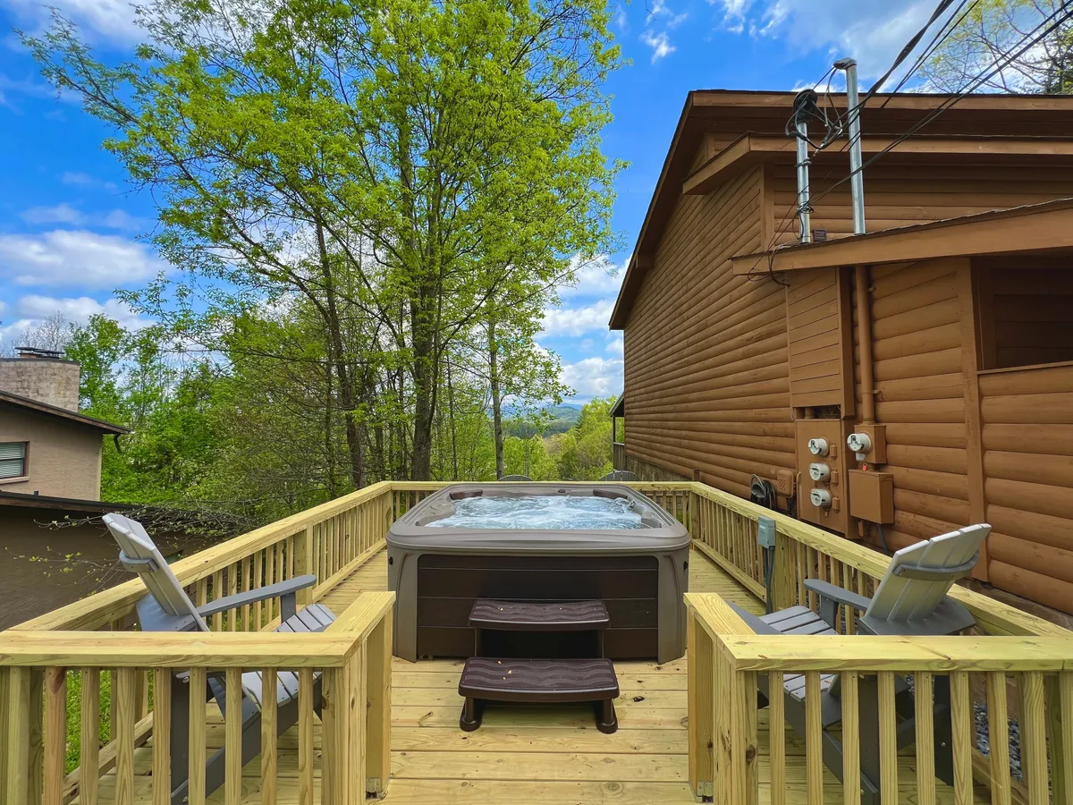 The image displays a spacious deck outfitted with a private hot tub and deck seating, surrounded by trees. The inviting setup is perfect for both social gatherings and quiet stargazing, reflecting a place where families can share memorable moments together outdoors.