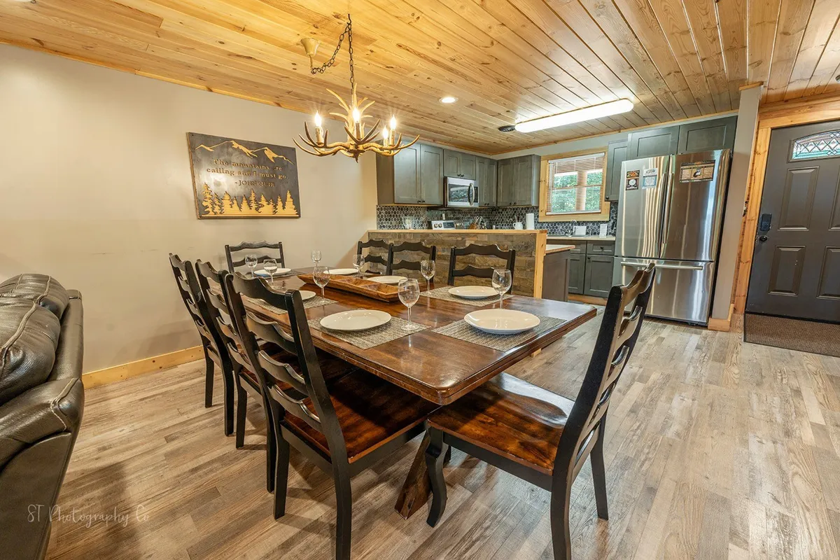This scene captures the seamless transition from the kitchen to the dining area, with a large dining table set beneath a stunning chandelier. The image includes views of both kitchen and dining spaces, highlighting their connection and the expansive table that seats groups comfortably.