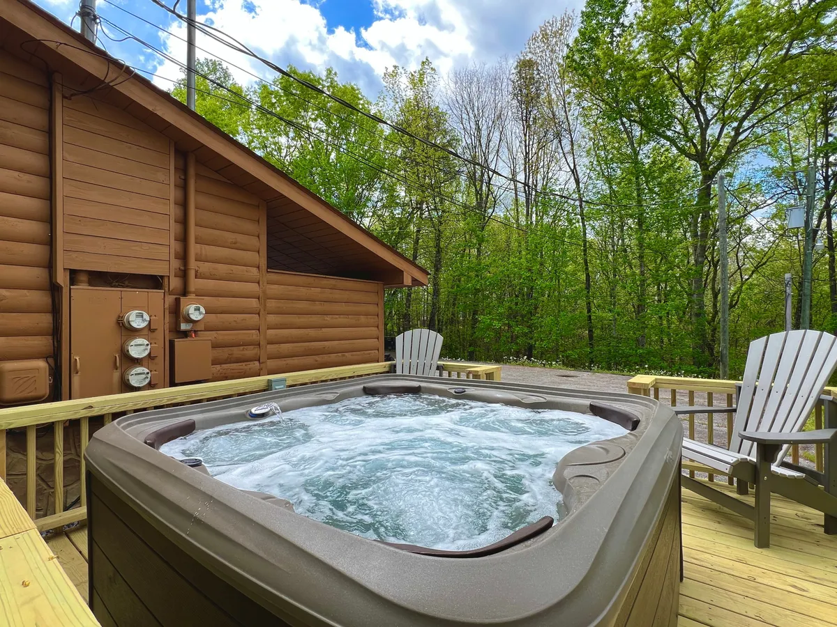 This image features a private hot tub on a spacious wooden deck, surrounded by lush trees. There are adirondack chairs positioned for relaxation, creating a tranquil outdoor oasis. The deck offers a sense of seclusion and direct access to nature, with warm lighting suggesting it’s perfect for sunset or evening enjoyment.
