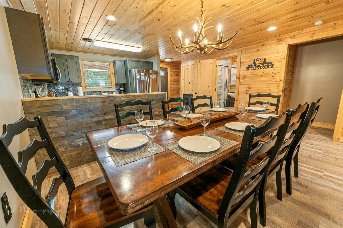 A warm dining space with a sturdy wooden table and a striking stone accent wall. Large windows frame glimpses of the outdoors, bringing in natural light and hinting at the beautiful landscape just beyond. The scene is perfect for communal gatherings and feels closely tied to the outdoors.