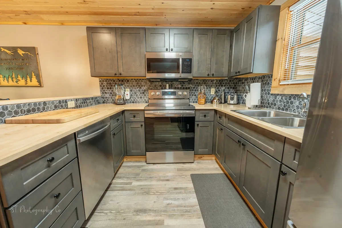 This image showcases a warm and inviting kitchen with stainless steel appliances, wooden countertops, and a stylish hexagonal tile backsplash. The layout highlights ample counter space, making it an ideal spot for group meal prep. The scene radiates a cozy, communal vibe and illustrates the kitchen’s role as a gathering hub.