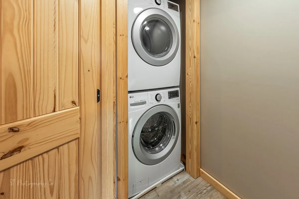 A practical laundry area with a stacked washer and dryer is set against wooden cabinetry and neutral walls, creating a homey, convenient space for extended stays.