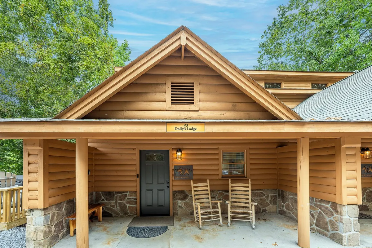 The image shows the wooden exterior of the lodge with inviting rocking chairs on the porch and a sign displaying the lodge's name. The porch looks out onto greenery, suggesting a peaceful, communal space that's perfect for relaxing after a day of family activities.