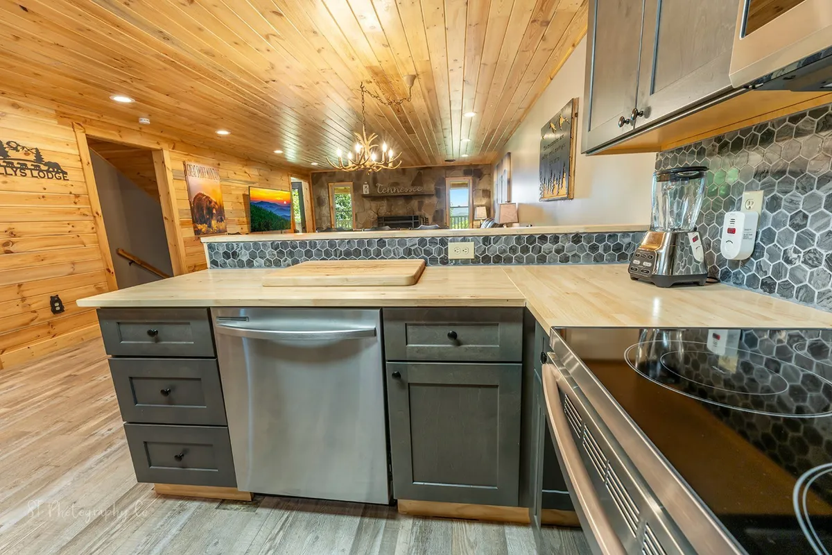 Here, the kitchen is presented from a different angle, focusing on a spacious kitchen island, more stainless steel appliances, and the warm ambiance created by wooden ceilings and a statement chandelier. The inviting design encourages group interaction and meal preparation together.