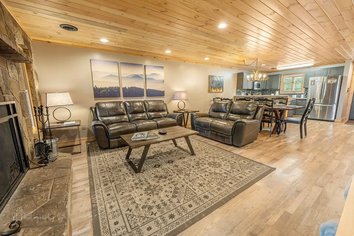 A warm, rustic living area with a stone fireplace, leather sofas, a coffee table topped with books, and thoughtfully chosen decorative artwork. The ambiance is cozy and inviting, ideal for gathering with friends or family.