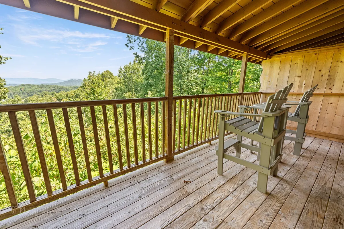 This exterior shot captures a wooden railing, outdoor chairs, and a sweeping view of the lush green landscape. It conveys tranquility and connection to the natural beauty of the Smokies, ideal for morning coffee or winding down with family stories under the stars.