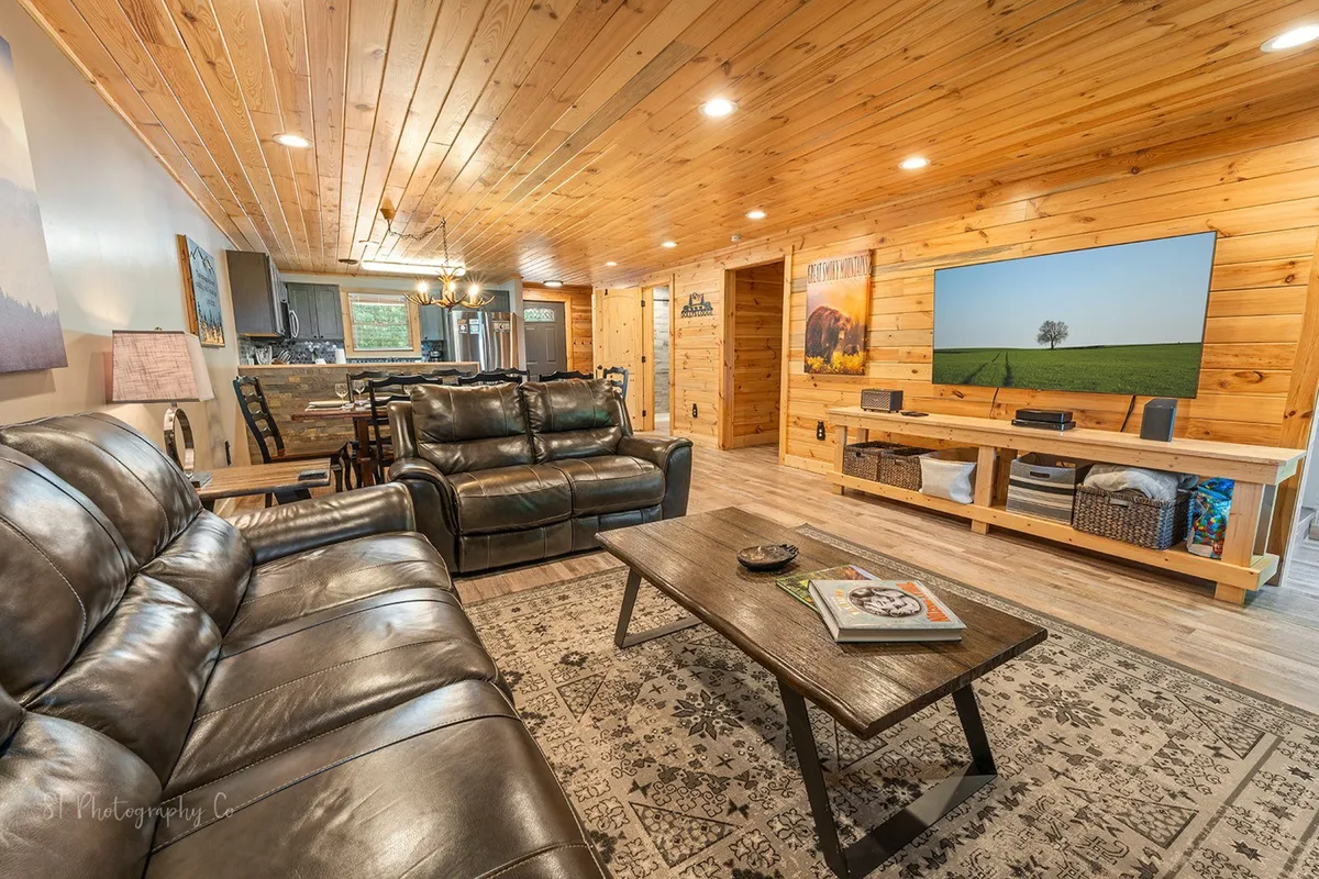 An inviting living space with comfortable leather sofas, a wooden ceiling, a flat-screen television, and a central coffee table. The arrangement encourages socializing, movie nights, or relaxing after mountain adventures, with modern amenities blending with rustic details.